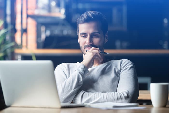 Man holding pen looking at laptop